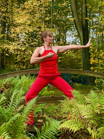 Brigitte Eisenmann von GESUNDMUNTER in roter Sportkleidung bei einer Qigong-Übung im Wald